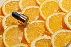 ein hell und erfrischend Anzeige von ein Vitamin c Serum Pipette neben frisch Orange Scheiben auf Orange Hintergrund. Hautpflege foto