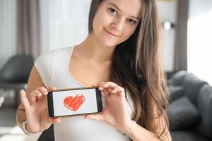 Welt Gesundheit Tag Konzept. jung Frau zeigen Illustration von Herz auf ihr Smartphone, illustrieren das Bedeutung von kardiovaskulär Gesundheit Bewusstsein auf International Gesundheit Überwachung foto