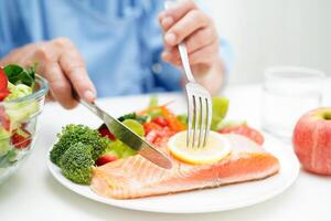 asiatisch Alten Frau geduldig Essen Lachs Anteil und Gemüse Salat zum gesund Essen im Krankenhaus. foto