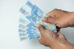 männlich Hand halten ein Menge von indonesisch Geld Rupiah auf ein isoliert Weiß Hintergrund. Geschäft Konzept , finanziell Konzept foto