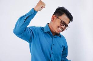 aufgeregt jung asiatisch Geschäftsmann im tragen Blau Hemd Stehen tun Gewinner Geste Zusammenpressen Fäuste isoliert auf Weiß Hintergrund foto