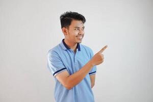 lächelnd asiatisch Mann mit Finger zeigen zu das Seite tragen Blau t Hemd isoliert auf Weiß Hintergrund foto