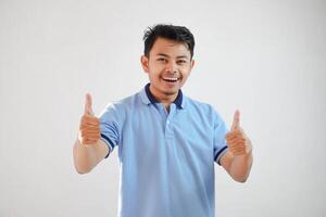 Porträt von heiter asiatisch Mann im tragen Blau t Hemd lächelnd und zeigen Daumen oben beim Kamera isoliert Über Weiß Hintergrund foto