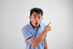 schockiert asiatisch Mann mit ein öffnen Mund mit Finger zeigen zu das Seite tragen Blau t Hemd isoliert auf Weiß Hintergrund foto