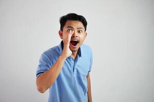 Porträt von ein jung asiatisch Mann schreiend aus laut mit Hand beim seine Mund tragen Blau t Hemd isoliert Über Weiß Hintergrund foto