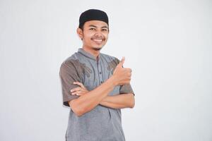 lächelnd oder glücklich jung Muslim Mann zeigen Hand Daumen oben tragen grau Muslim Kleider isoliert auf Weiß Hintergrund foto