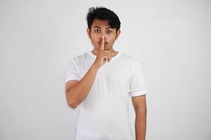 ernst jung asiatisch Mann zeigen Stille Geste mit Finger tragen Weiß t Hemd isoliert auf Weiß Hintergrund foto