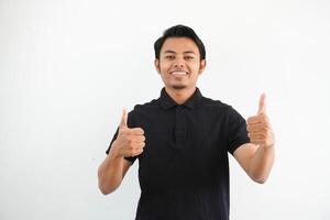 glücklich oder lächelnd jung asiatisch Mann geben zwei Daumen oben tragen schwarz Polo t Hemd isoliert auf Weiß Hintergrund foto