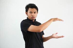 jung asiatisch Mann posieren auf ein Weiß Hintergrund schockiert und erstaunt halten ein Kopieren Raum zwischen Hände, tragen schwarz Polo t Shirt. foto