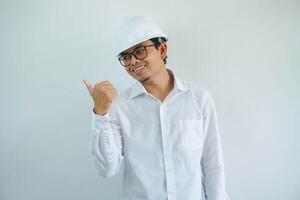 jung asiatisch Architekt Mann tragen Baumeister Sicherheit Helm Über isoliert Hintergrund lächelnd mit glücklich Gesicht suchen und zeigen zu das Seite mit Daumen hoch. foto