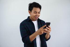 lächelnd jung asiatisch Mann suchen zu seine Handy, Mobiltelefon Telefon mit glücklich Ausdruck isoliert auf Weiß Hintergrund foto