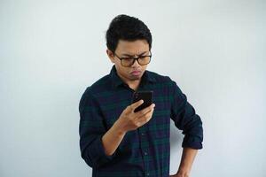 ernst jung asiatisch Mann suchen diese Telefon mit Hände auf Taille isoliert auf Weiß Hintergrund foto