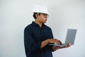 ernst jung asiatisch Architekt Mann tragen Baumeister Sicherheit Helm Tippen auf das Laptop isoliert auf Weiß Hintergrund foto