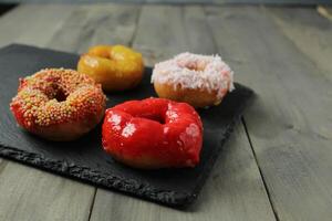 vier bunt glasiert Donuts Lügen auf ein schwarz Tablett grau Hintergrund foto