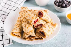 dünn Pfannkuchen gerollt in Rollen mit Beere Marmelade auf ein Teller auf das Tabelle foto