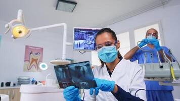 geduldig pov im Dental Büro Planung Chirurgie Schritte von Zähne Hohlraum, Zahnarzt zeigen auf Röntgen Bild. Stomatologie Arzt tragen schützend Maske und Handschuhe, Arbeiten im modern stomatologisch Klinik foto