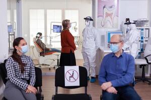 Senior Frau mit Gesicht Maske diskutieren mit Zahnarzt gekleidet mit ppe passen im Stomatologie Klinik, wie Sicherheit Vorsicht während global Pandemie mit Coronavirus. foto