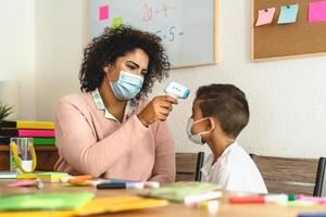 Lehrer Frau Untersuchung Temperatur auf Kind im Klassenzimmer während Corona Virus Pandemie - - Gesundheitswesen medizinisch und Bildung Konzept foto