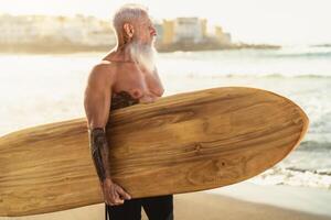 Fitness Senior haben Spaß Surfen beim Sonnenuntergang Zeit - - sportlich bärtig Mann Ausbildung mit Surfbrett auf das Strand - - Alten gesund Menschen Lebensstil und extrem Sport Konzept foto