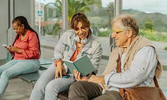gemischtrassig Menschen lesen ein Buch während warten beim Straßenbahn Bahnhof im das Stadt foto