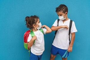 Kinder tragen Gesicht schützend Maske gehen zurück zu Schule während Corona Virus Pandemie - - wenig Kinder tun Neu Sozial Entfernung Gruß stoßen Ellbogen - - Gesundheitswesen und Bildung Konzept foto