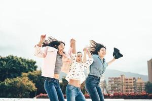 glücklich asiatisch Mädchen Springen zusammen draussen - - jung Frauen freunde haben Spaß während Universität brechen Tanzen und feiern draußen - - tausendjährig Generation, Freundschaft und Jugend Menschen Lebensstil foto