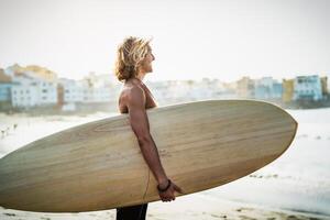 passen jung Mann haben Spaß Surfen während Sonnenuntergang Zeit - - glücklich Surfer männlich halten Surfbrett auf das Strand - - Jugend Menschen Lebensstil und extrem Sport Konzept foto