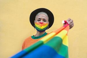 jung Frau tragen Fröhlich Stolz Maske halten Regenbogen Flagge Symbol von lgbtq Sozial Bewegung foto