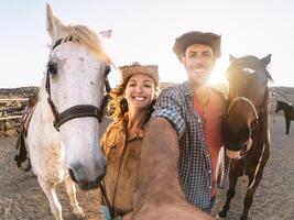 glücklich Paar nehmen Selfie mit Pferde Innerhalb stabil - - jung Bauern haben Spaß mit Tiere im Corral Ranch - - Mensch und Tiere Beziehung Lebensstil Konzept foto