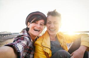 glücklich Fröhlich Paar nehmen Selfie auf das Strand beim Sonnenuntergang - - jung Lesben haben Spaß Dating zuerst Zeit - - LGBT, Homosexualität Liebe und Beziehung Lebensstil Konzept foto