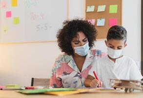Lehrer Frau mit Kind tragen Gesicht schützend Maske im Vorschule Klassenzimmer während Corona Virus Pandemie - - Gesundheitswesen und Bildung Konzept foto