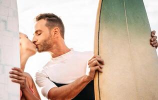 glücklich Surfer Paar küssen Vor Surfen im das Ozean - - romantisch Liebhaber Datum haben zärtlich Romantik Momente draussen - - Liebe Beziehung und Sport Menschen Lebensstil Konzept foto