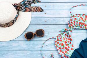 oben Aussicht von ein Stroh Weiß Hut mit Brille und ein Badeanzug, Lügen auf ein Blau hölzern hintergrund.sommer Ferien Konzept foto