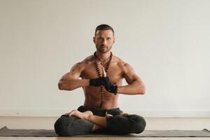 ein Mann mit ein nackt Torso ist Sitzung im das Lotus Position Vor tun Yoga drinnen. Fitness Trainer foto