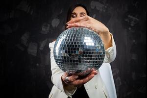 Porträt von ein Frau halten ein Silber Disko Ball. genommen im ein Foto Studio.