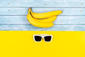 Gelb Bananen und Sonnenbrille Lüge auf ein Blau hölzern Hintergrund und ein Gelb Hintergrund foto