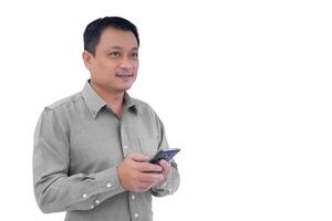 Erwachsene asiatisch Geschäft Mann ist halten Smartphone Handy, Mobiltelefon Telefon im seine Hand und aussehen aus während isoliert Weiß Hintergrund. foto