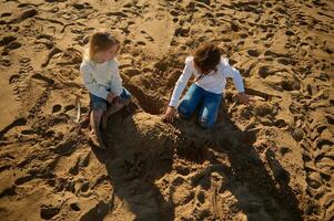 zwei wenig Mädchen, Schwester Sitzung auf das Strand und Gebäude ein Sand Schloss. Konzept von das Familie Urlaub. foto