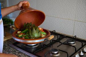 Nahansicht von ein Hausfrau Kochen Gemüse im Tajine Lehm Gericht beim Zuhause Küche foto