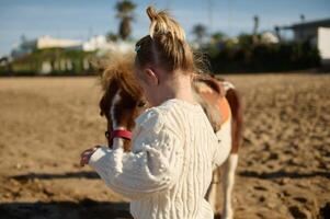 Rückseite Aussicht von ein wenig Kind Mädchen mit ein Pony auf das sandig Strand foto