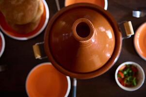 oben Aussicht Lehm Topf Tajine, frisch gebacken brechen und leeren sauber Orange Platten auf hölzern Tisch. marokkanisch traditionell Essen foto