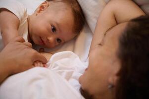 Nahansicht von ein süß Baby Lügen Nächster zu seine Mutter während sie Stillen ihn. foto