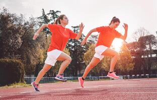 sportlich Mädchen Laufen auf Wettbewerb - - jung Frauen tun trainieren Session auf Spur beim Sonnenuntergang draussen - - Menschen, gesund, Fitness und Sport Lebensstil Konzept foto