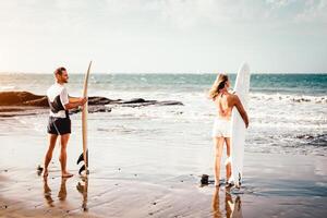 Paar von Surfer Stehen auf das Strand mit Surfbretter vorbereiten zu Surfen auf hoch Wellen - - sportlich jung Menschen haben Spaß während ein Surfen Tag - - extrem Sport, Beziehung und Jugend Lebensstil Konzept foto