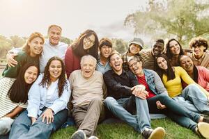 glücklich Mehrgenerationenhaus Menschen haben Spaß Sitzung auf Gras im ein Öffentlichkeit Park foto