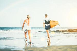 jung Surfer Paar Laufen mit Surfbretter im das Wasser während Sonnenuntergang - - gesund sportlich freunde genießen das Tag zum Surfen - - Konzept von Menschen, Sport, extrem und Lebensstil foto