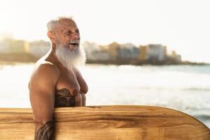 passen Senior männlich haben Spaß Surfen während Sonnenuntergang Zeit - - im Ruhestand Mann Ausbildung mit Surfbrett auf das Strand - - Alten gesund Menschen Lebensstil und extrem Sport Konzept foto