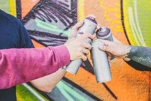 schließen oben Hände von Menschen halten Farbe sprühen Büchsen gegen das Graffiti Mauer - - Graffiti Künstler beim Arbeit - - Rebellen, Lebensstil, Straße Kunst Konzept - - Fokus auf können sprühen auf das richtig foto