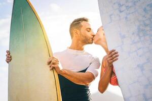 Gesundheit jung Paar von Surfer küssen beim Sonnenuntergang auf das Strand halten Surfbretter - - glücklich Liebhaber haben ein zärtlich Moment mit ein Kuss während Surfen zusammen - - Menschen, Liebe, Sport und Lebensstil Konzept foto