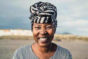 glücklich Muslim afrikanisch Frau tragen Turban lächelnd im Kamera auf das Strand während Sommer- Ferien foto